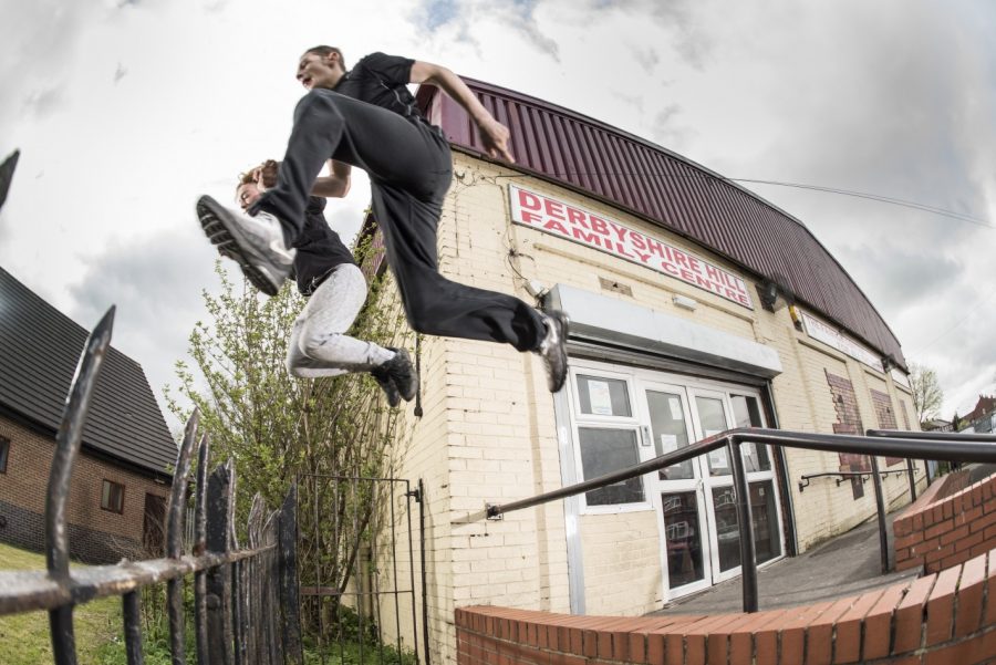 Two free runners are in motion jumping over a spiked fence.