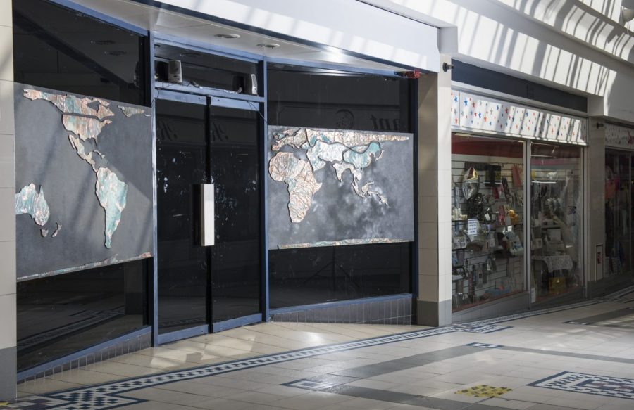 A shop window inside a shopping centre. On the window are two maps. The windows and doors are otherwise blacked out.